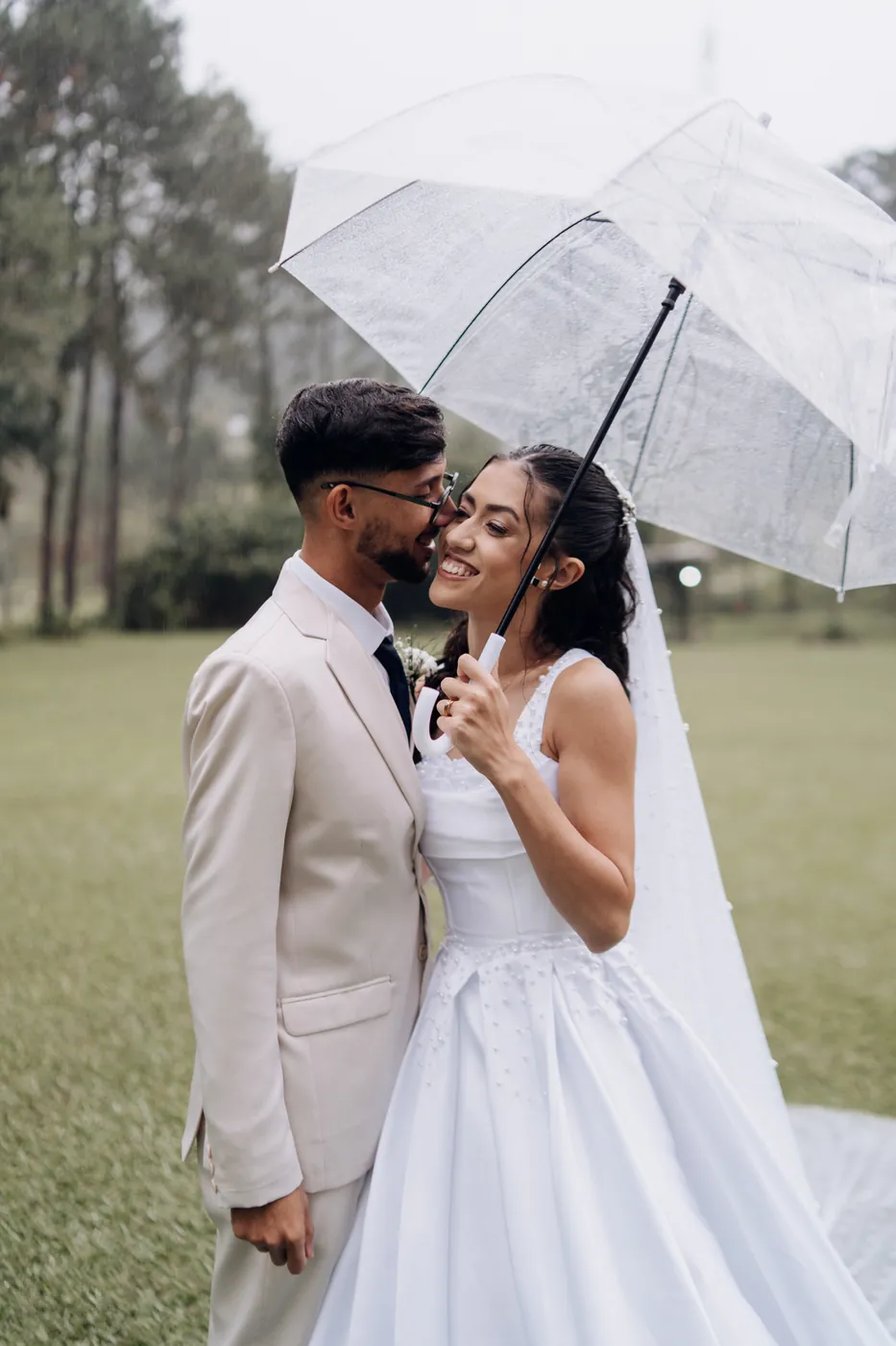 Noiva sorrindo com guarda-chuva transparente ao lado do noivo