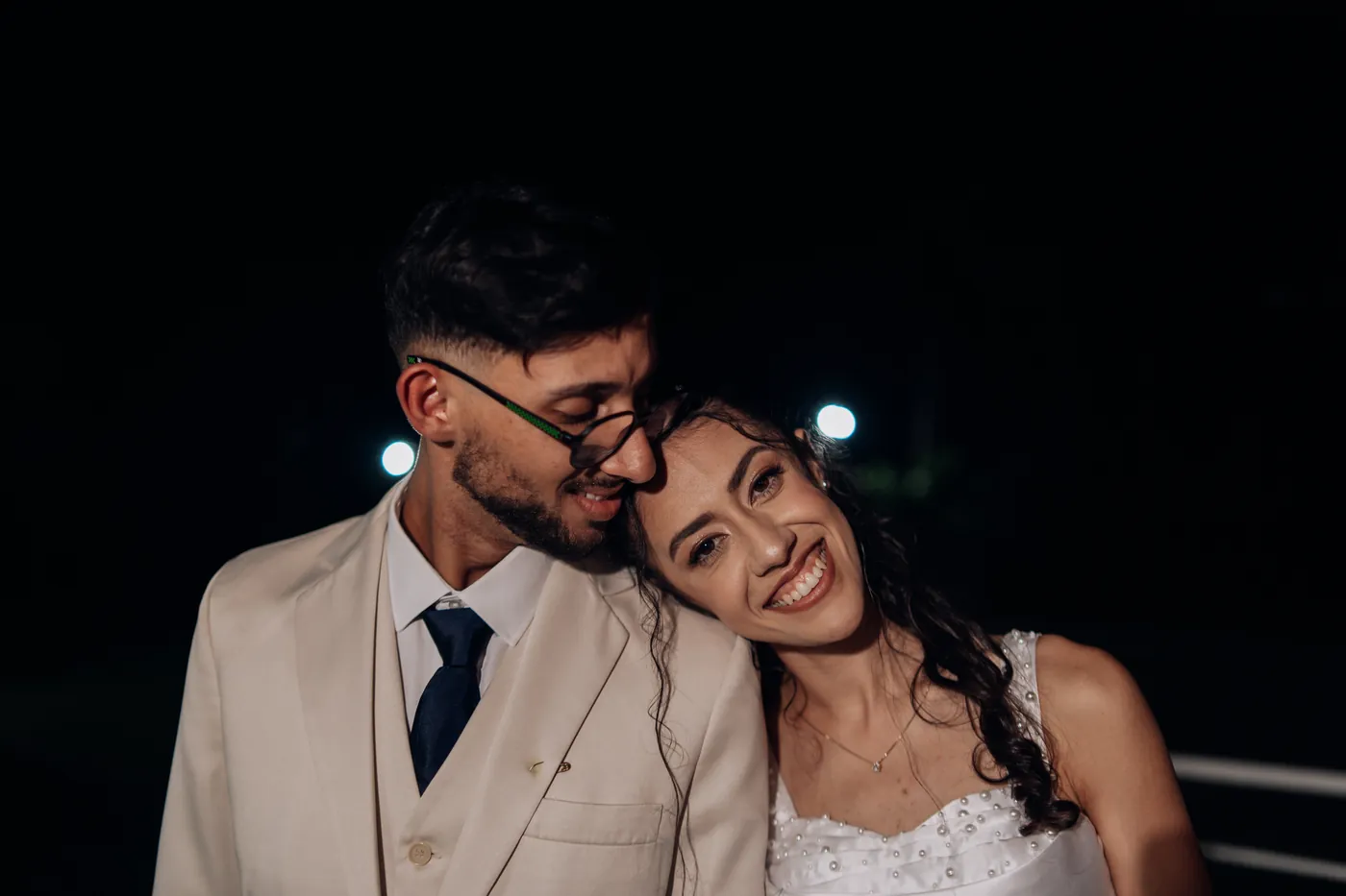 Noivos sorrindo abraçados à noite